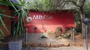 Eine rote Wand mit dem Namen 'ARENSIG' und dekorativen Elementen, darunter eine Vogel-Skulptur, Steine und eine kleine Pflanze.