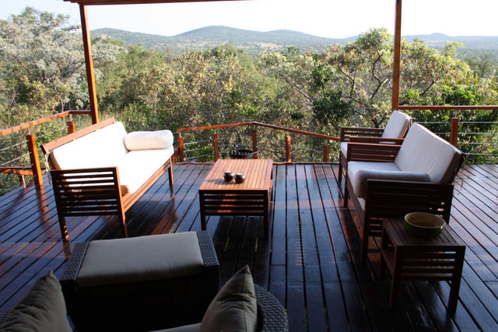 Una terraza de madera con mobiliario exterior, incluyendo un sofá y sillas, con vistas a un paisaje montañoso.