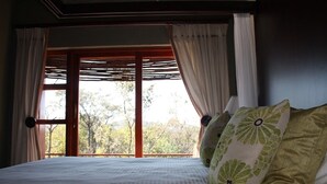 Ein Schlafzimmer mit großem Fenster, einem Bett mit weißer Bettdecke und zwei Kissen mit Blumenmuster.