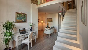 A modern interior with a staircase, a desk with a laptop, a chair, a potted plant, and two paintings on the walls.