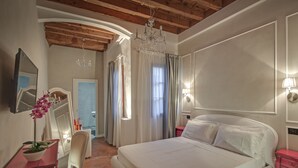 A bedroom with a large bed, a desk with a chair, a mirror, and a chandelier.