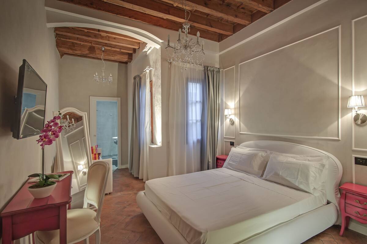 Ein Schlafzimmer mit einem großen Bett, einem Schreibtisch mit Stuhl, einem Spiegel und einer Chandelier.
