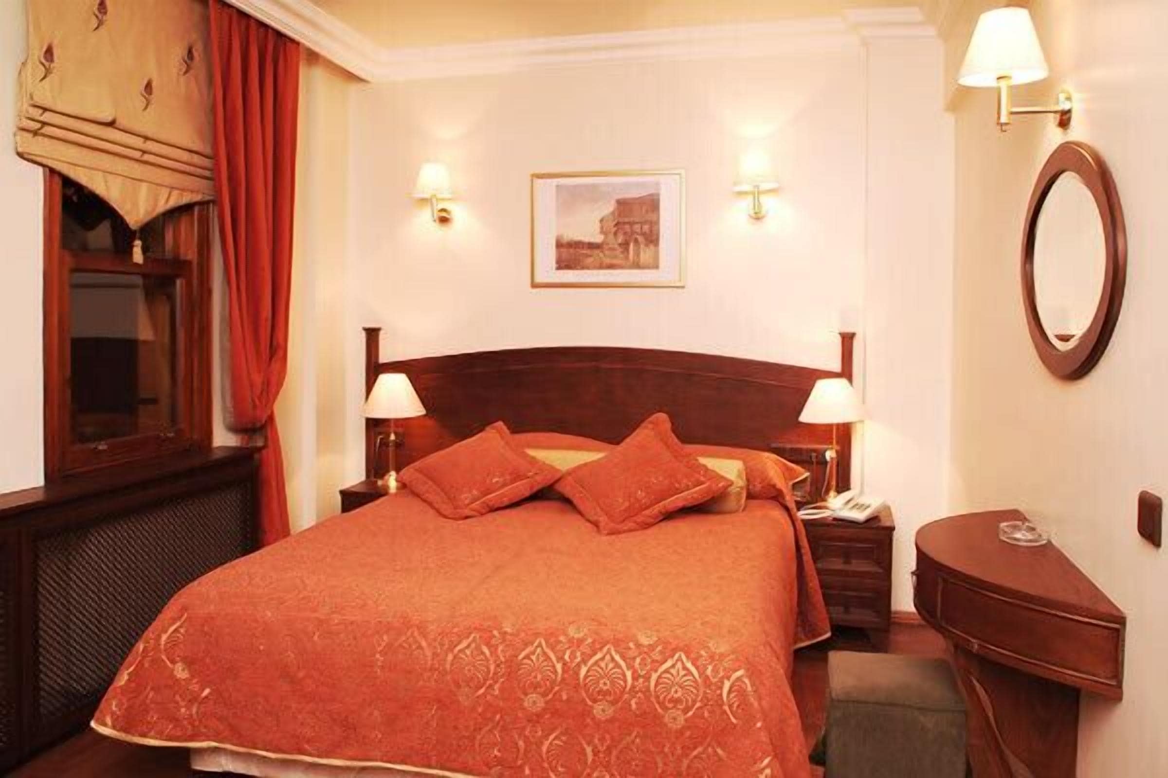A hotel room with a large bed, two bedside lamps, a small bedside table, a mirror, and a framed picture on the wall.