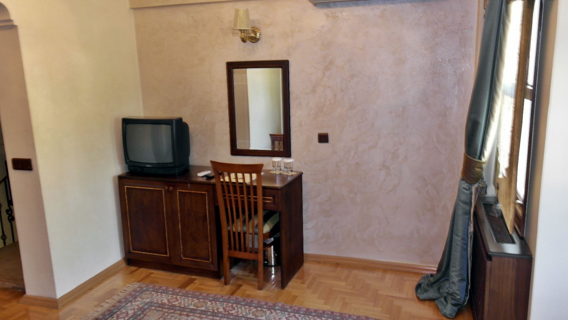 A small room with a wooden cabinet, a television, a chair, a mirror, and a patterned rug.