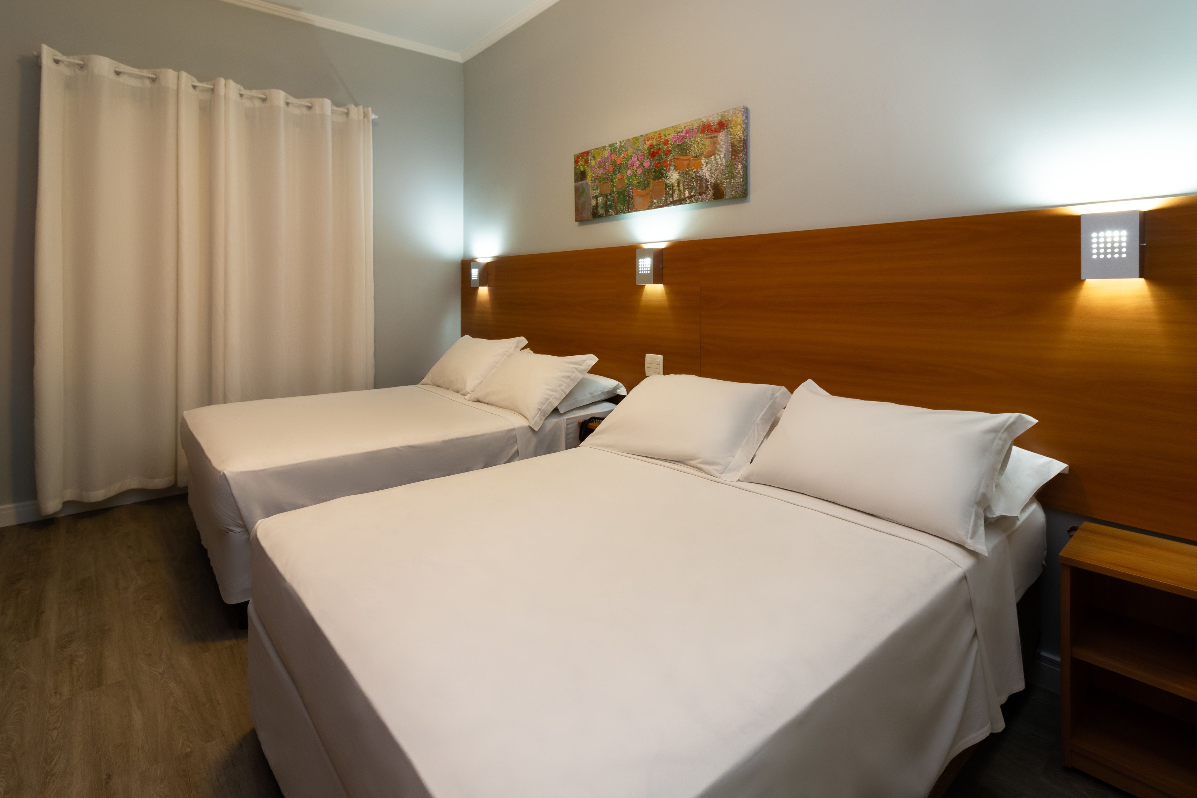 A hotel room with two single beds, a wooden headboard, a painting on the wall, and a nightstand.
