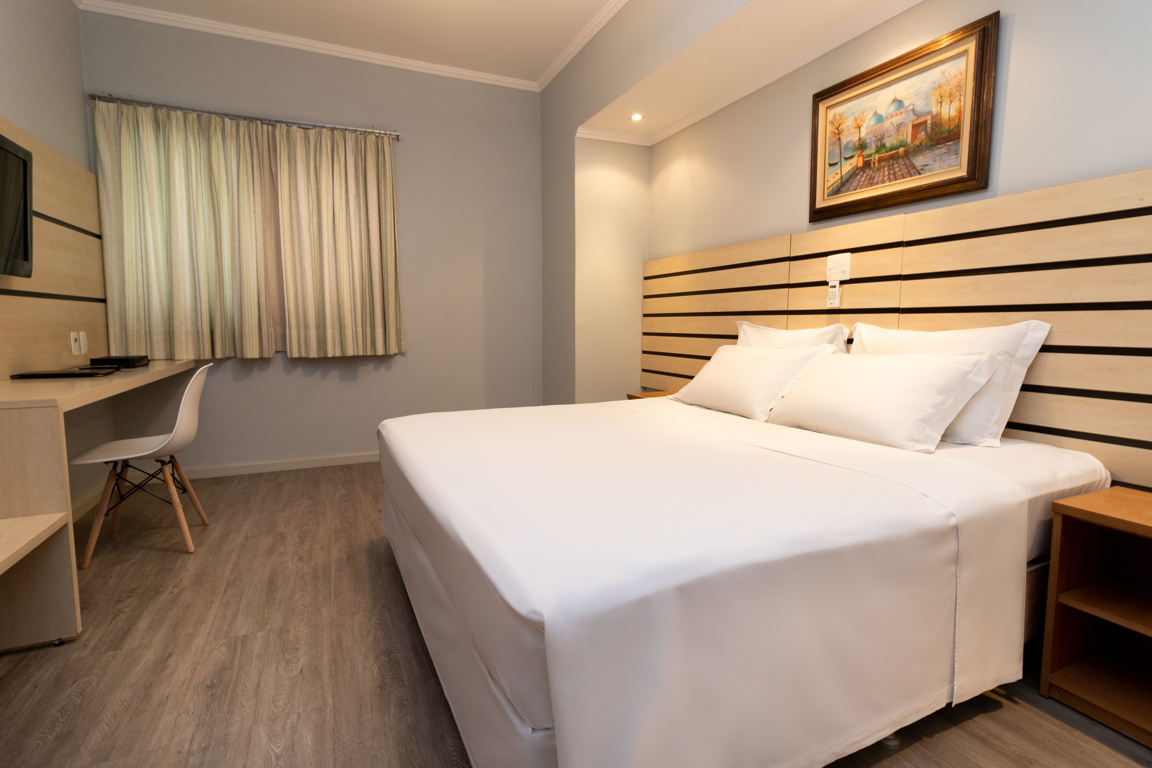 Une chambre d’hôtel avec un grand lit, un bureau, une chaise et un tableau au mur.