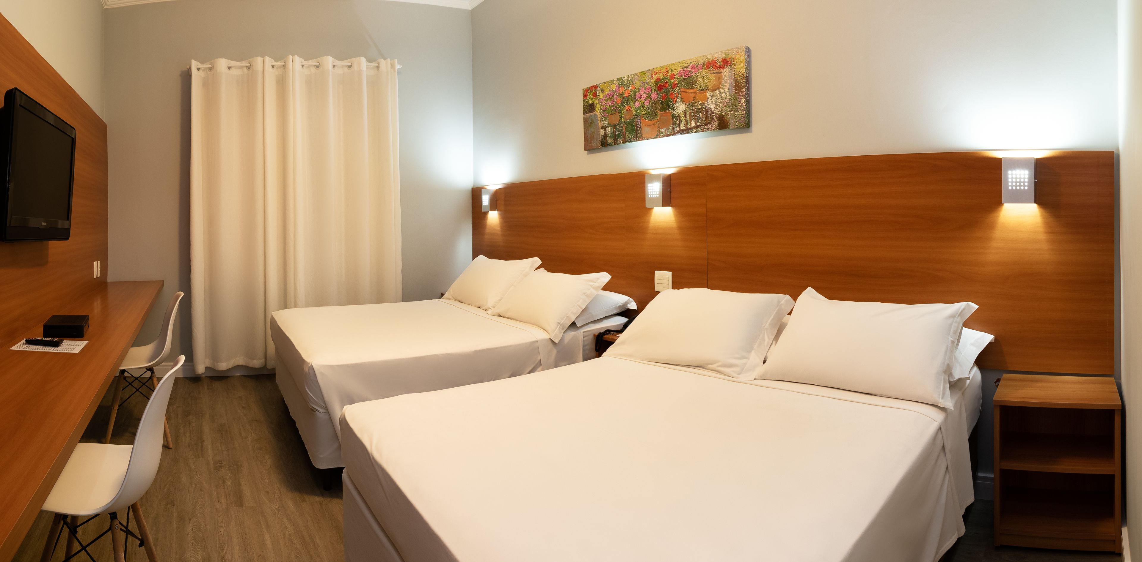 Een hotelkamer met twee bedden, een houten hoofdeinde, een schilderij, een televisie, een bureau en een stoel.