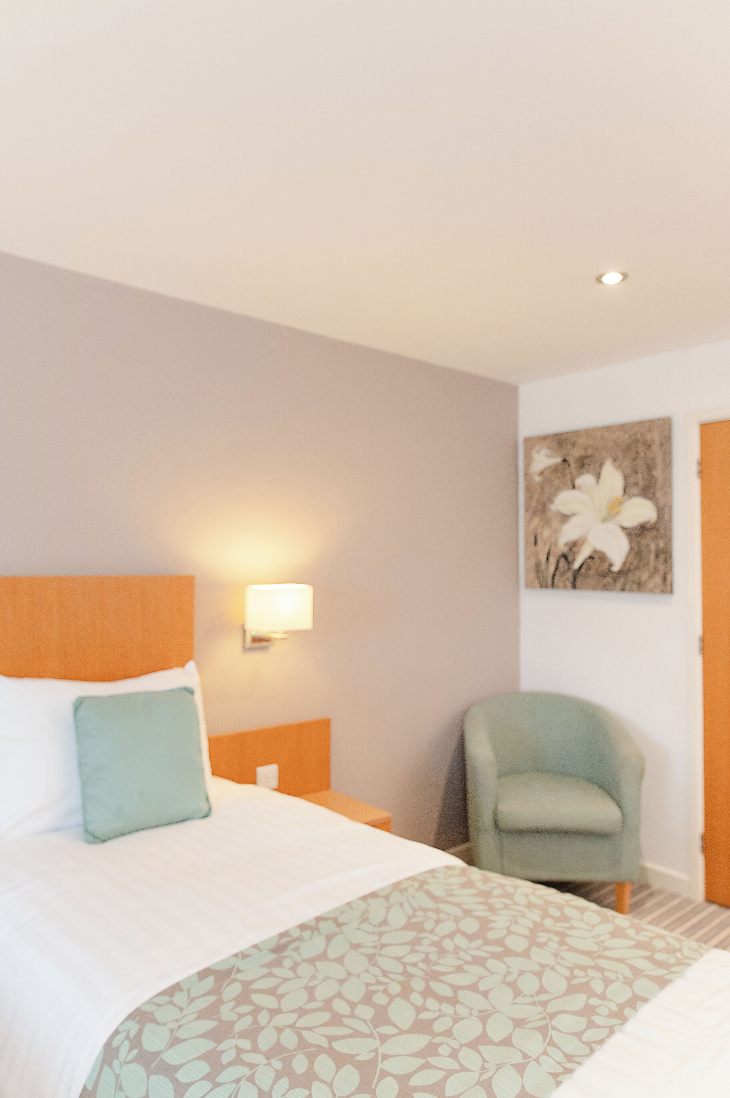 Una habitación de hotel con una cama, una mesita de noche, una lámpara de pared, una silla y un cuadro.