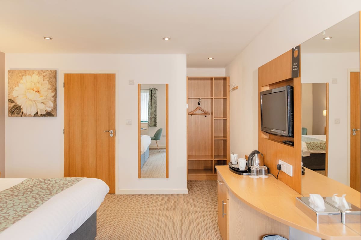 A hotel room with a bed, a desk with a TV, a mirror, a wardrobe, and a bathroom visible through an open door.