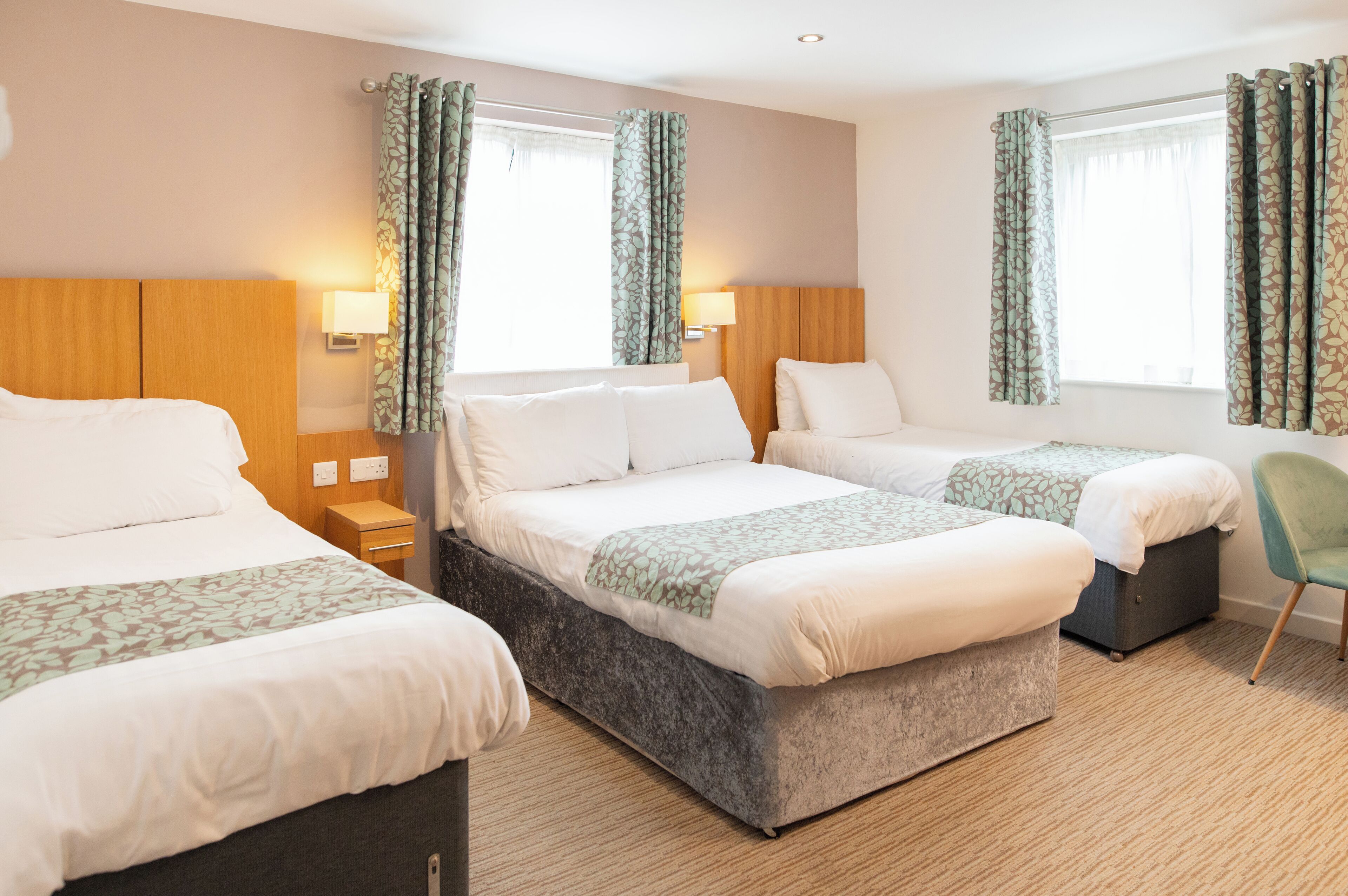 A hotel room with two beds, a bedside table, a chair, and a window with curtains.