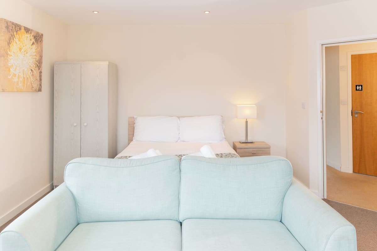 A bedroom with a bed, a nightstand, a wardrobe, and a door with an icon indicating a bathroom.