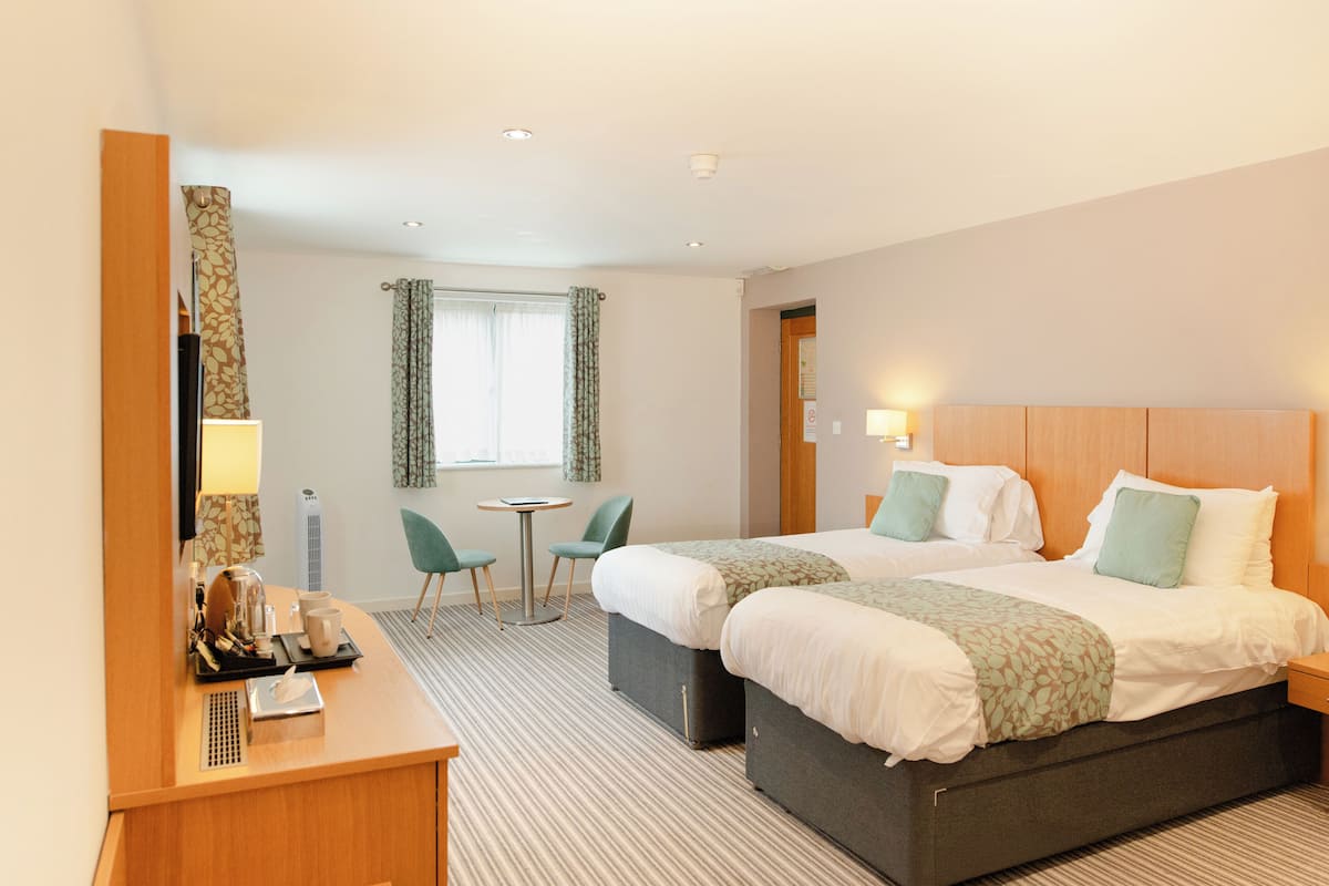 A hotel room with two beds, a desk with a coffee maker, a small table, and a chair.