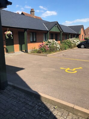 Una hilera de edificios de ladrillo con puertas y ventanas verdes, un estacionamiento con espacio reservado para discapacitados y un automóvil estacionado allí.
