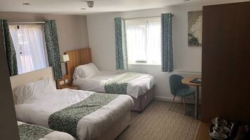 A hotel room with two beds, a desk, a chair, and a window with curtains.