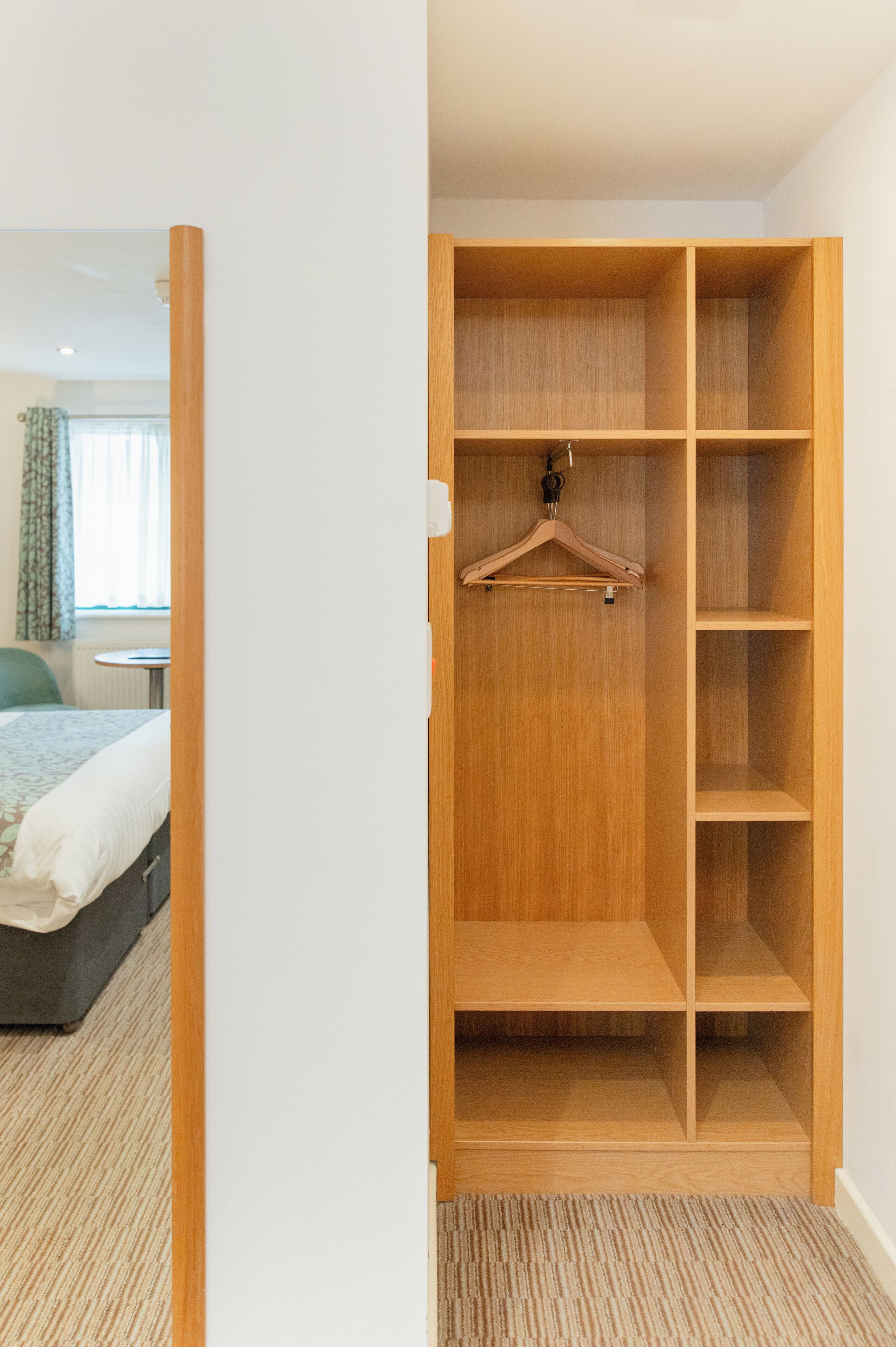A hotel room with a wooden wardrobe, a bed, a small table, and a chair.