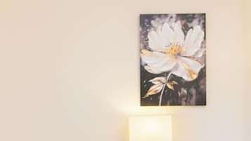 Une chambre d’hôtel avec un lit, une table de chevet avec une lampe, une commode et une œuvre d’art représentant une fleur, accrochée au mur.