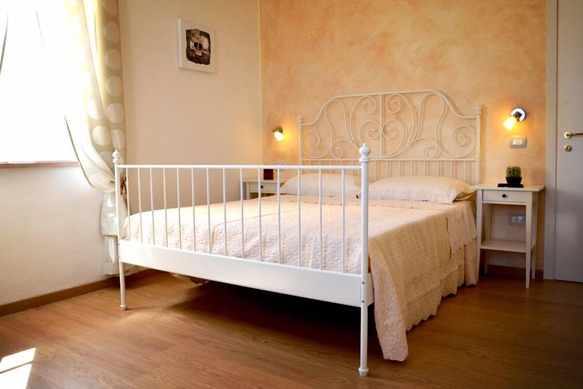 A single-bed room with a white metal frame, a beige bedspread, two bedside tables with lamps, and a door to the right.