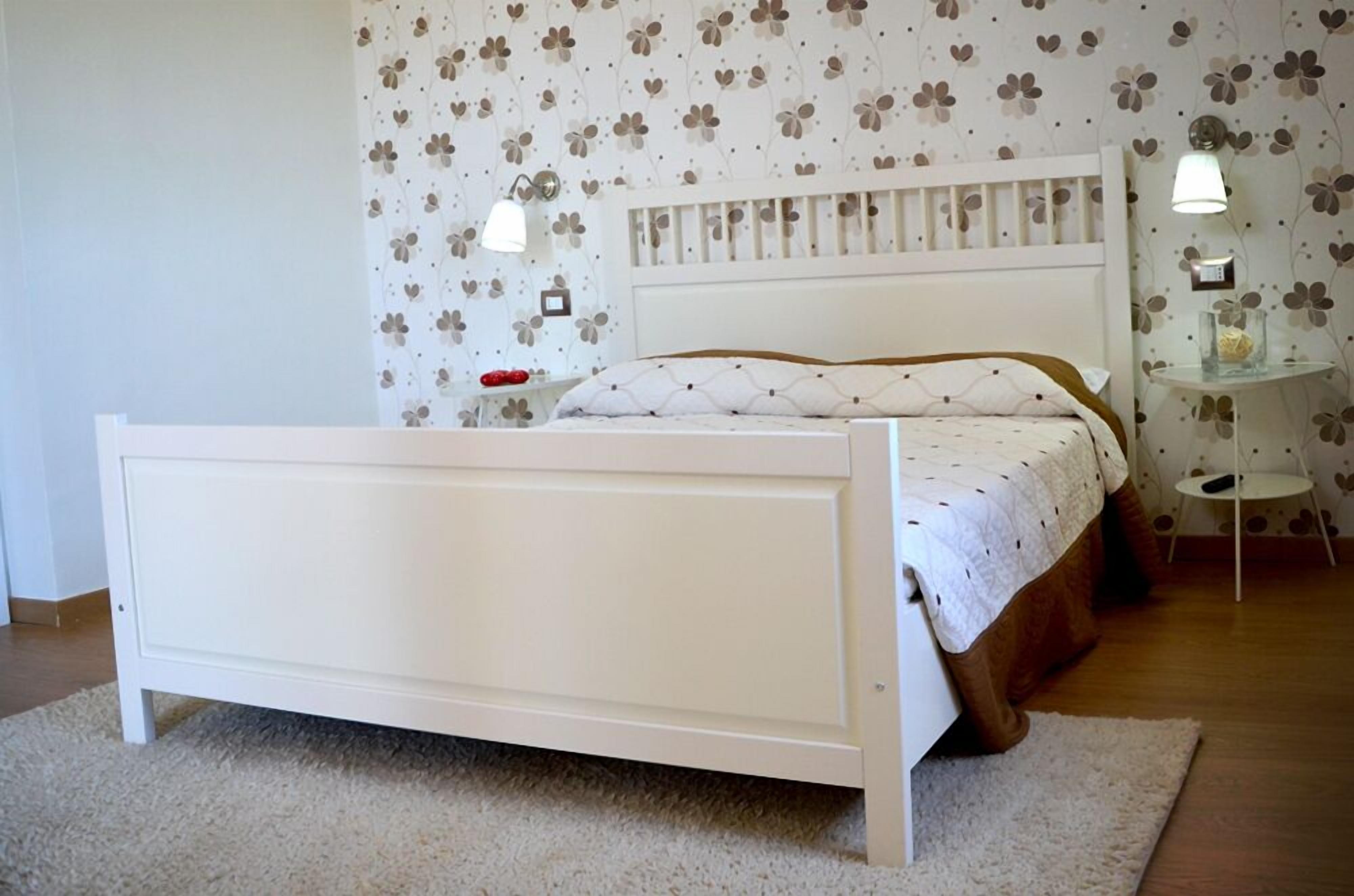 Un dormitorio con cama blanca, papel tapiz floral y lámparas de noche.