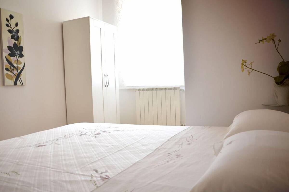 A bedroom with a bed, a wardrobe, a window with a view, and a wall-mounted artwork.