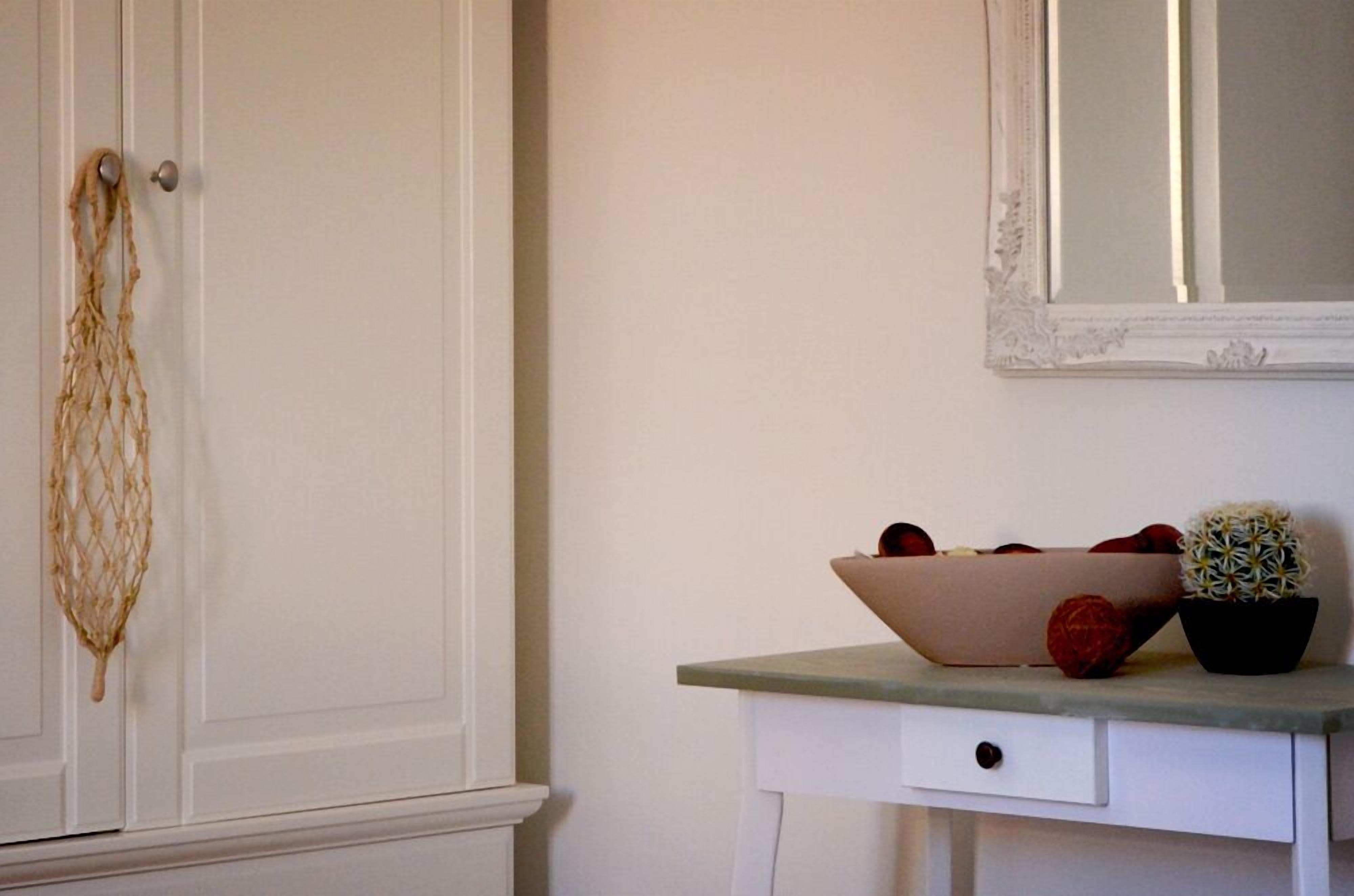 A white door with a rope hanging on the handle, a white dresser with a mirror above it, and a bowl of fruit on the dresser.