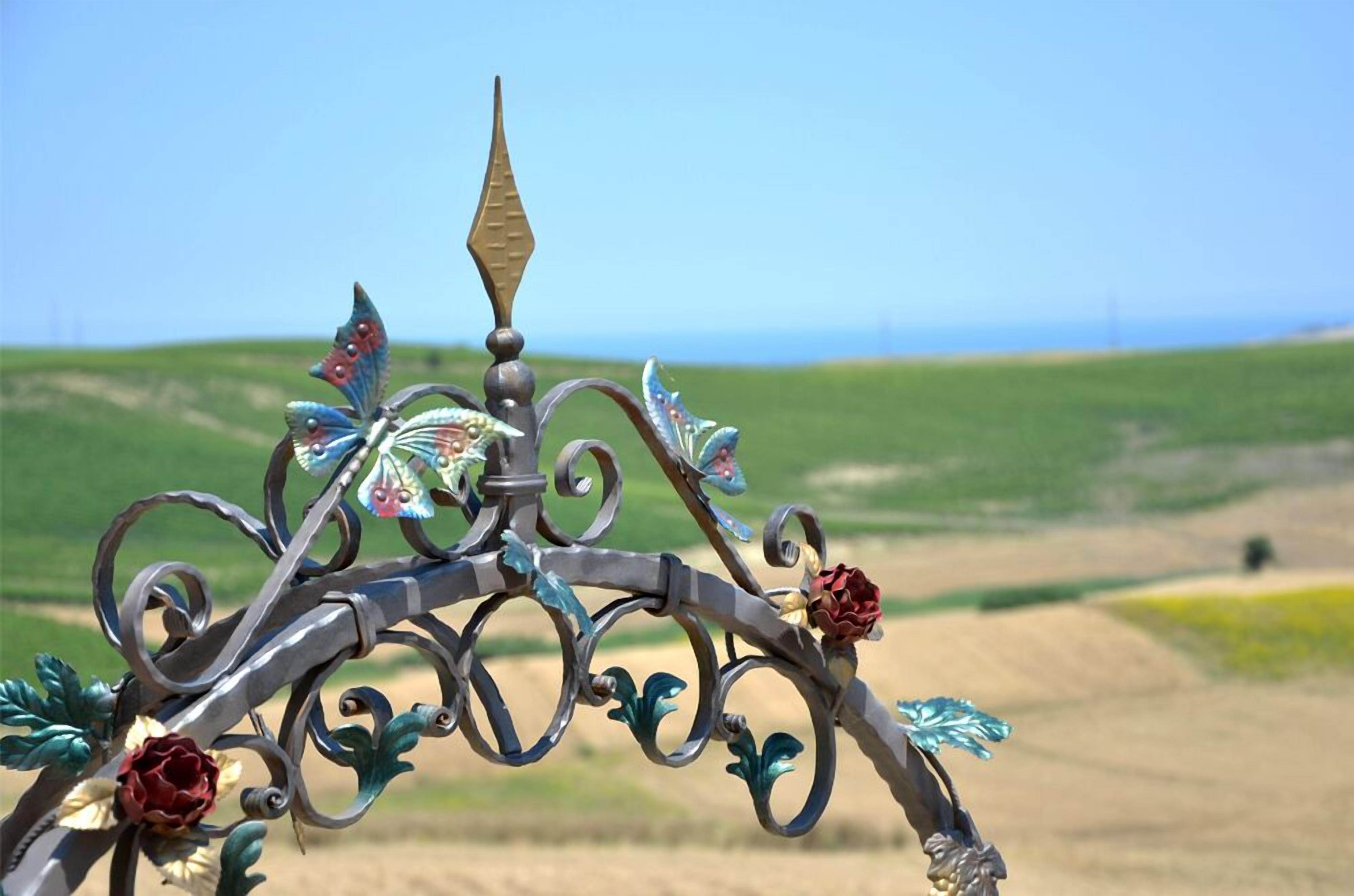 Un portail en fer forgé orné de motifs floraux et de feuilles, se dressant sur fond de paysage rural.