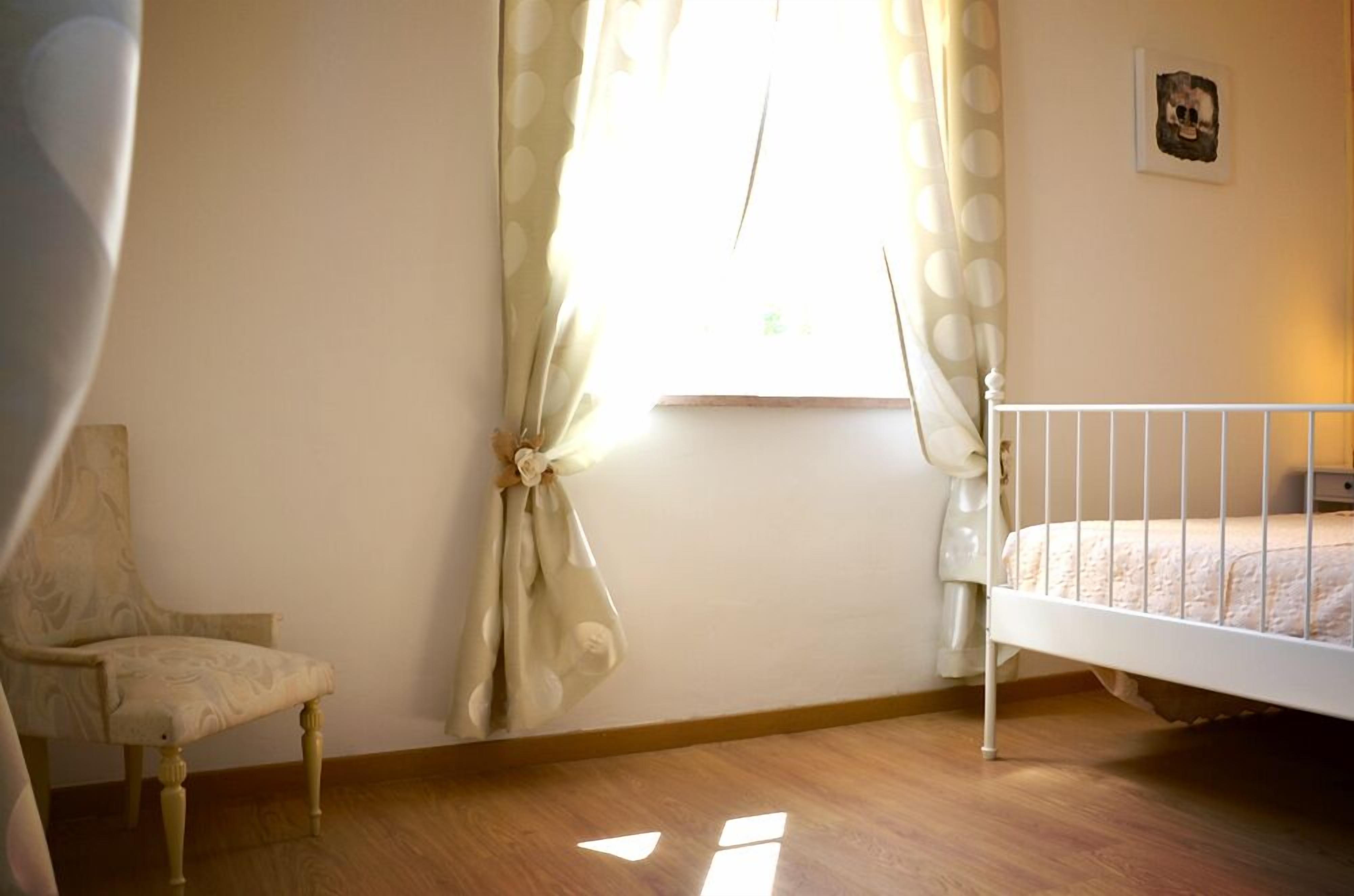 Un dormitorio con una cama individual, una silla y un ventanal con cortinas.