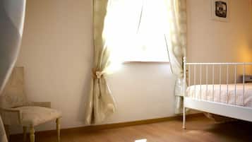 Un dormitorio con una cama individual, una silla y un ventanal con cortinas.