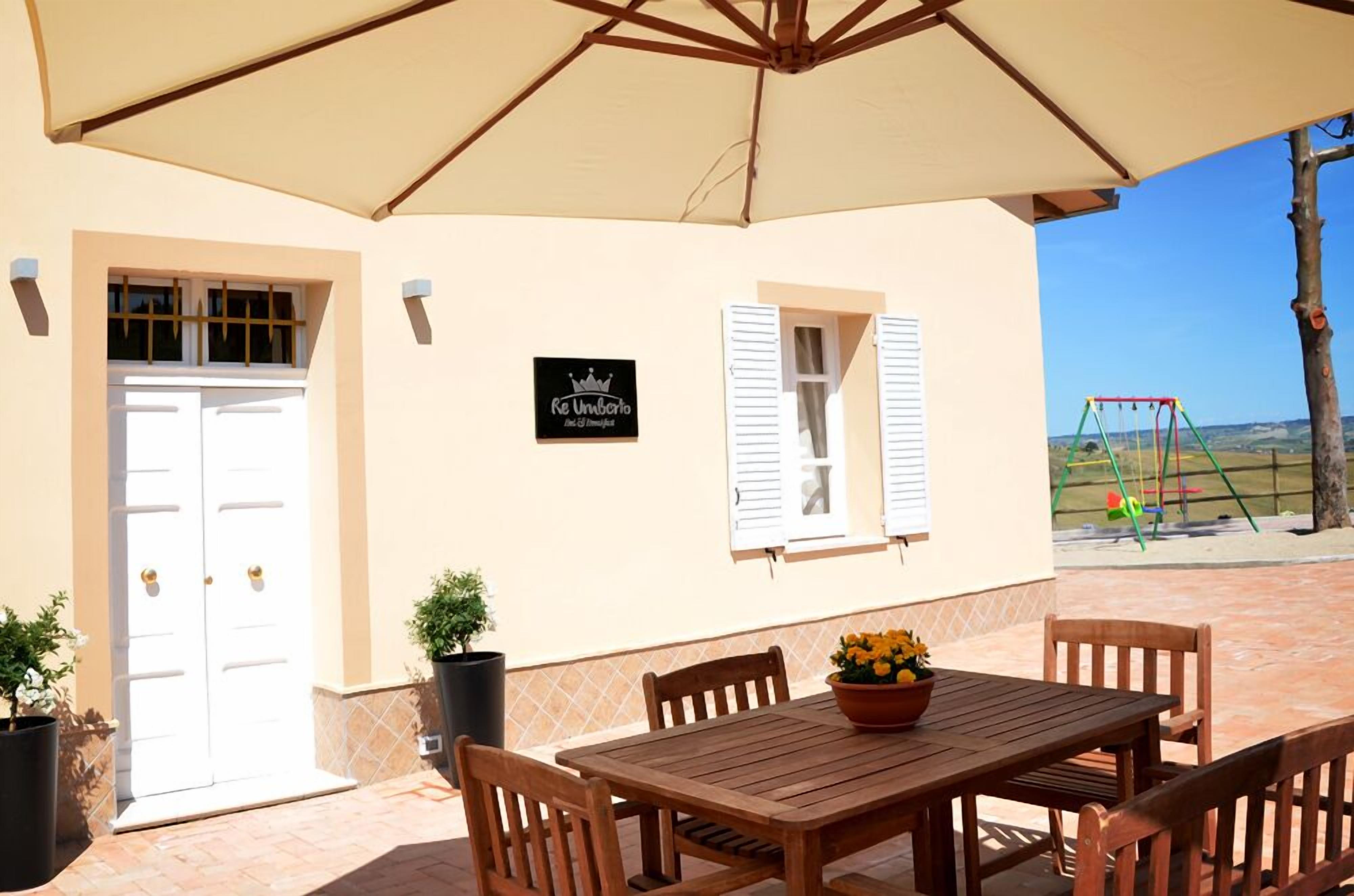 Eine Terrasse mit einem Holztisch und -stühlen, eine beige Wand mit einem Schild sowie eine Schaukel im Hintergrund.