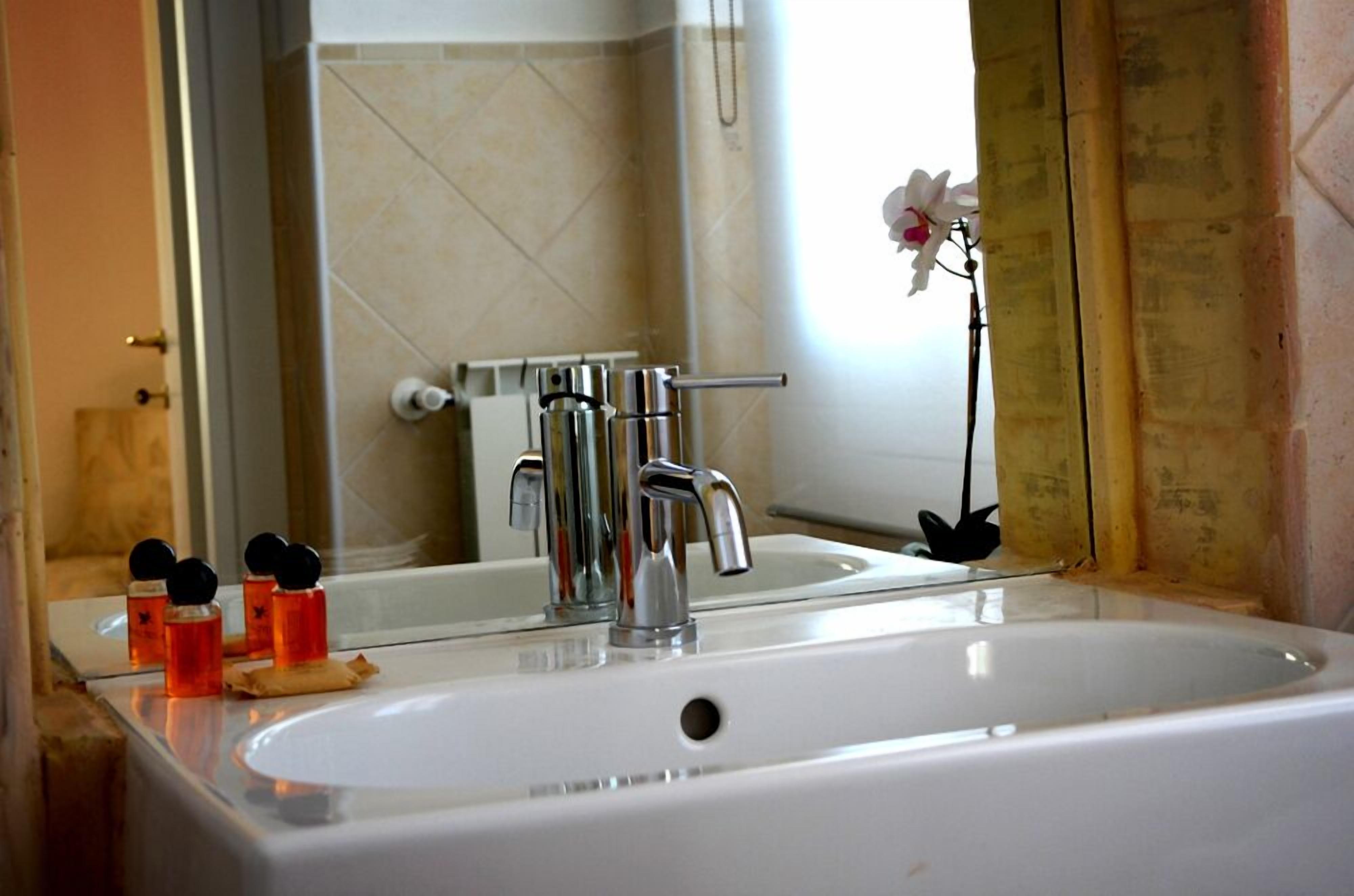 Un bagno con un lavandino bianco di grandi dimensioni, un rubinetto cromato e uno specchio che riflette la zona doccia.