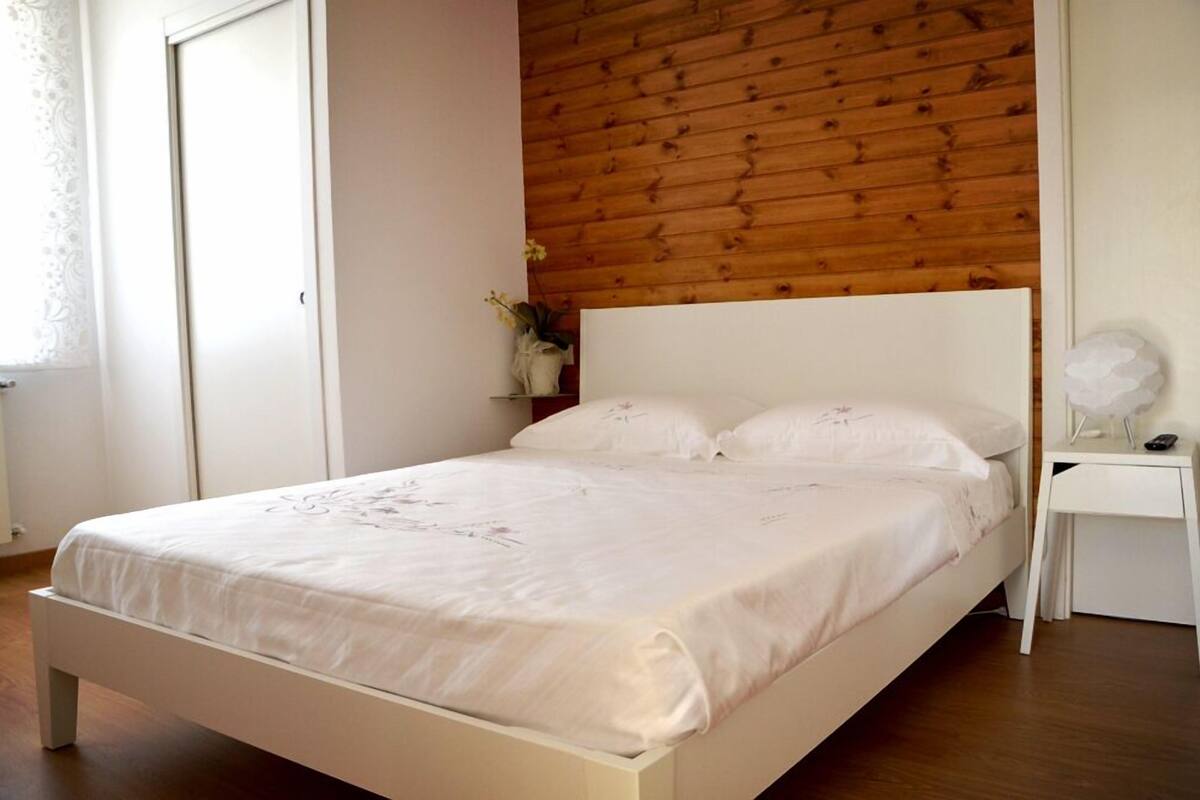 A bedroom with a wooden headboard, a white bed, and a nightstand with a lamp.
