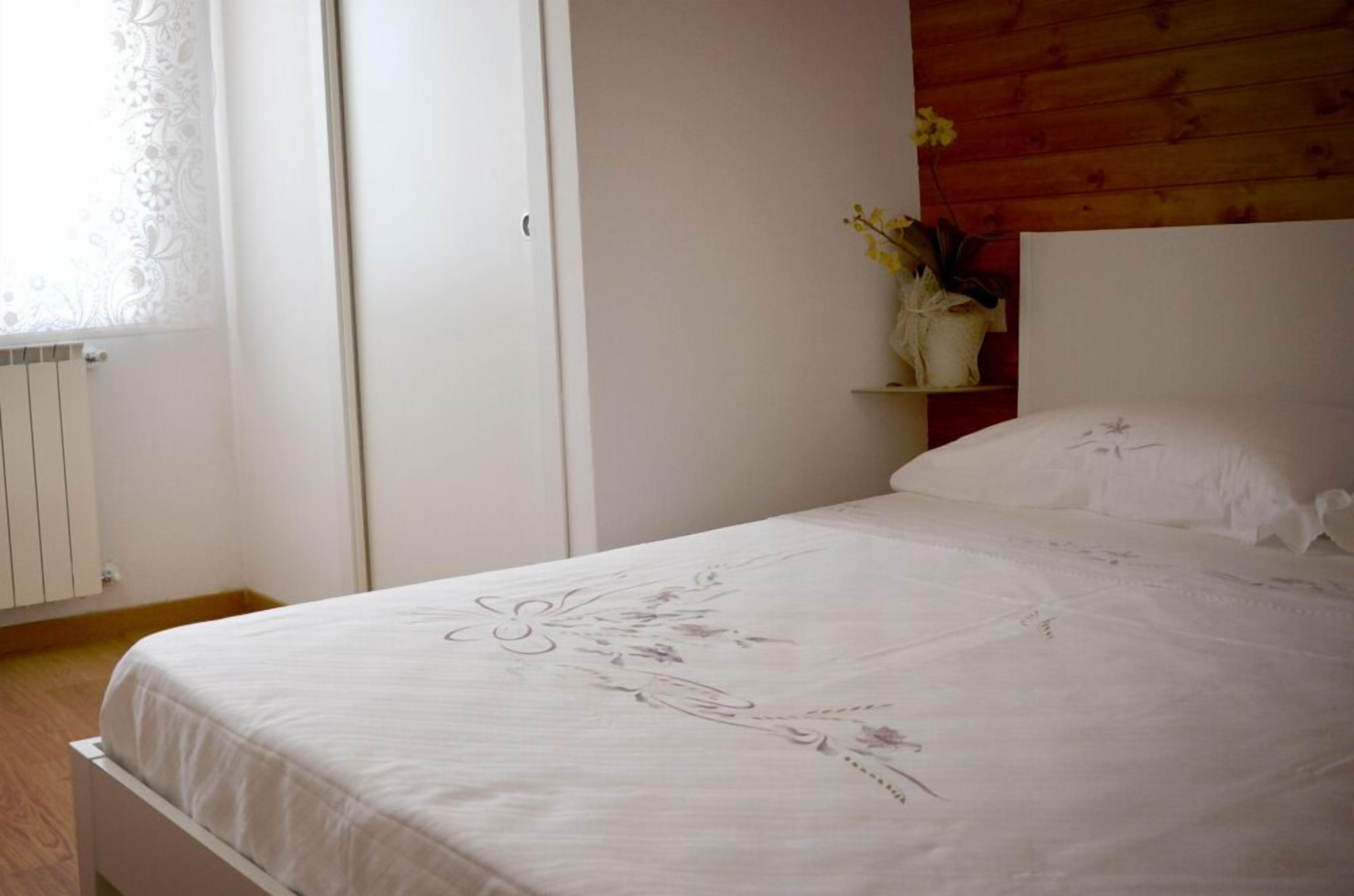 Ein Schlafzimmer mit einem Bett, einem weißen Kleiderschrank, einem Holzkopfteil und einem kleinen Regal mit einer Blumenvase.