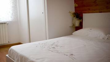 Ein Schlafzimmer mit einem Bett, einem weißen Kleiderschrank, einem Holzkopfteil und einem kleinen Regal mit einer Blumenvase.