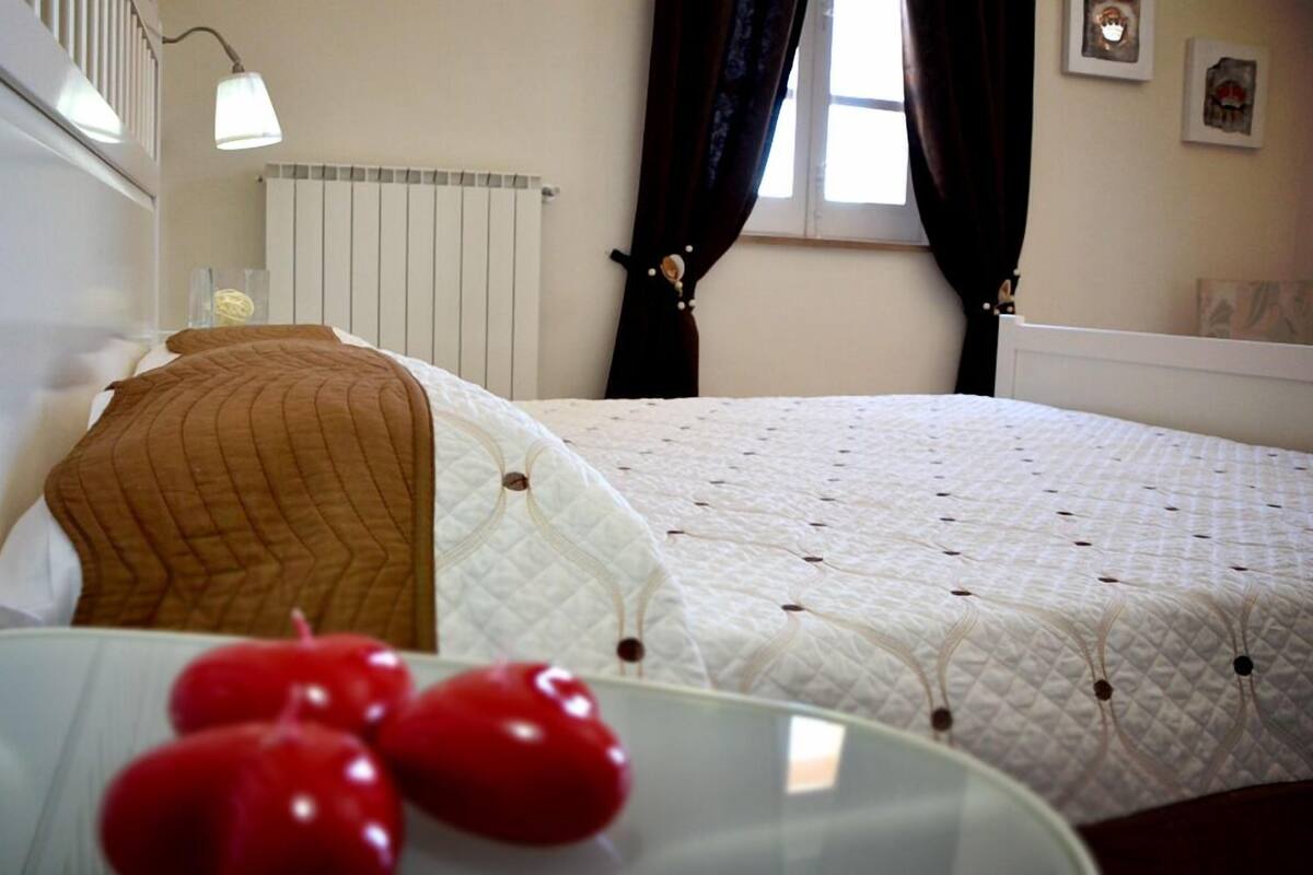 A bedroom with a bed, a bedside table with a glass top, and a window with curtains.