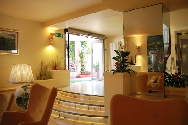 A hotel lobby with a staircase leading to a garden area, a reception desk, and several seating areas.