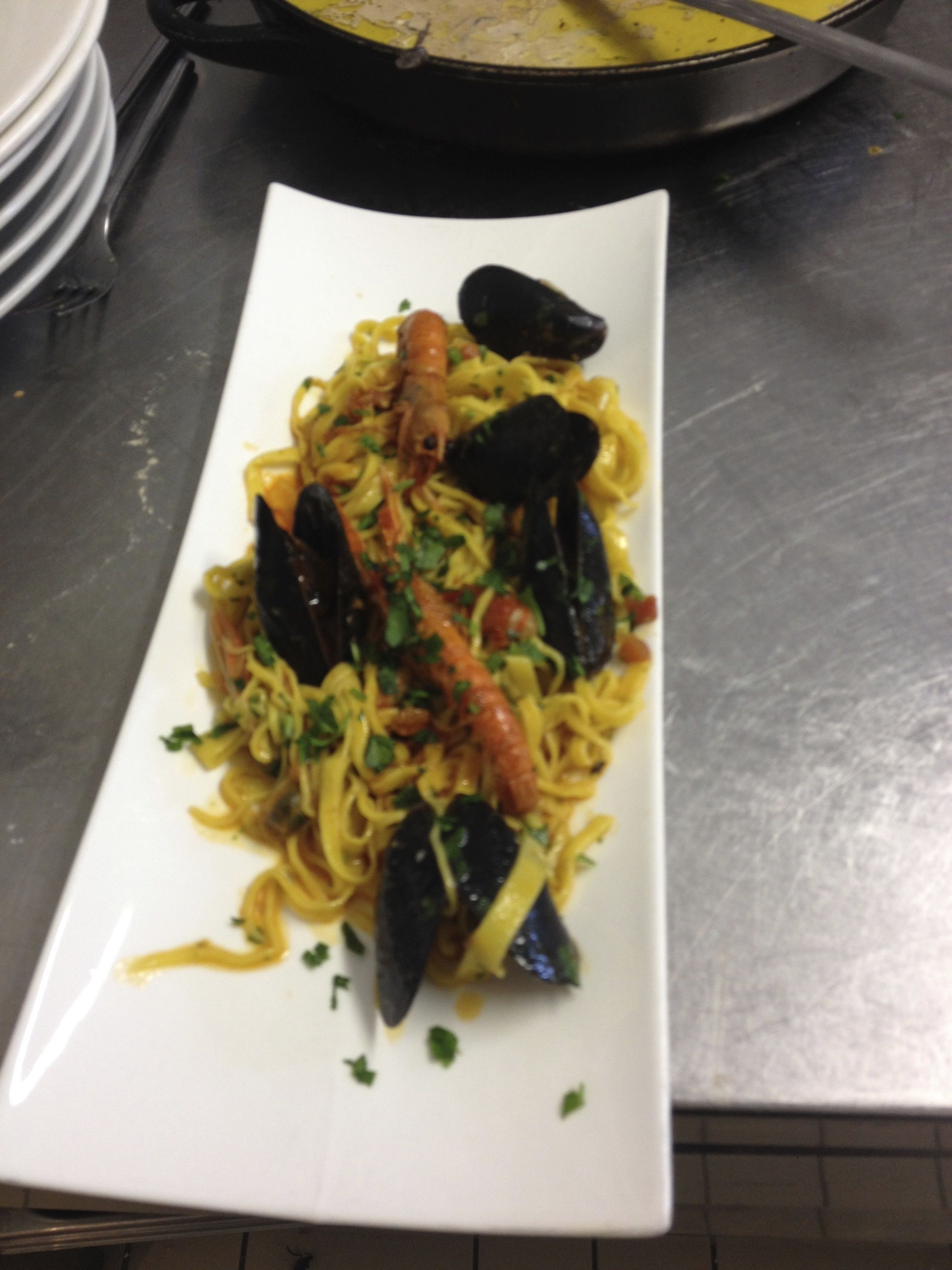 A rectangular white plate with pasta, mussels, and shrimp.