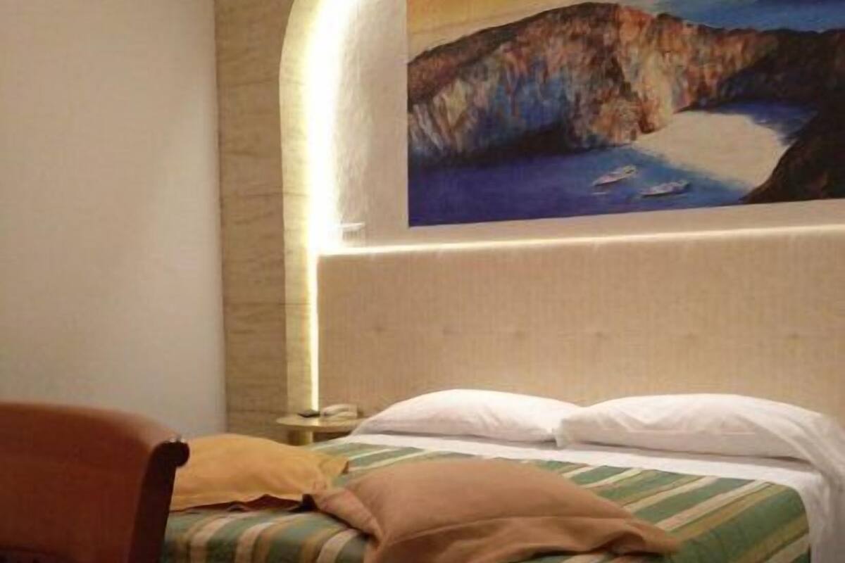 Une chambre d’hôtel avec un lit, une chaise et un tableau représentant un paysage côtier accroché au mur.