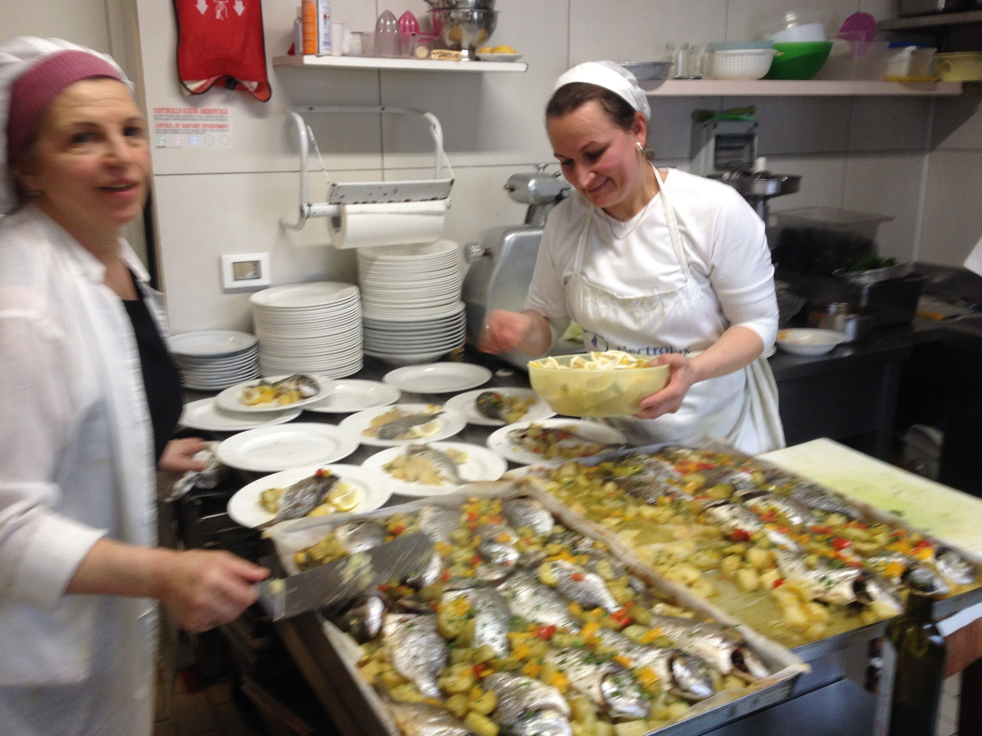 A kitchen with chefs preparing food, including fish and vegetables on trays.