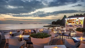 An outdoor seating area with tables and chairs, a bar, and a view of the sea.