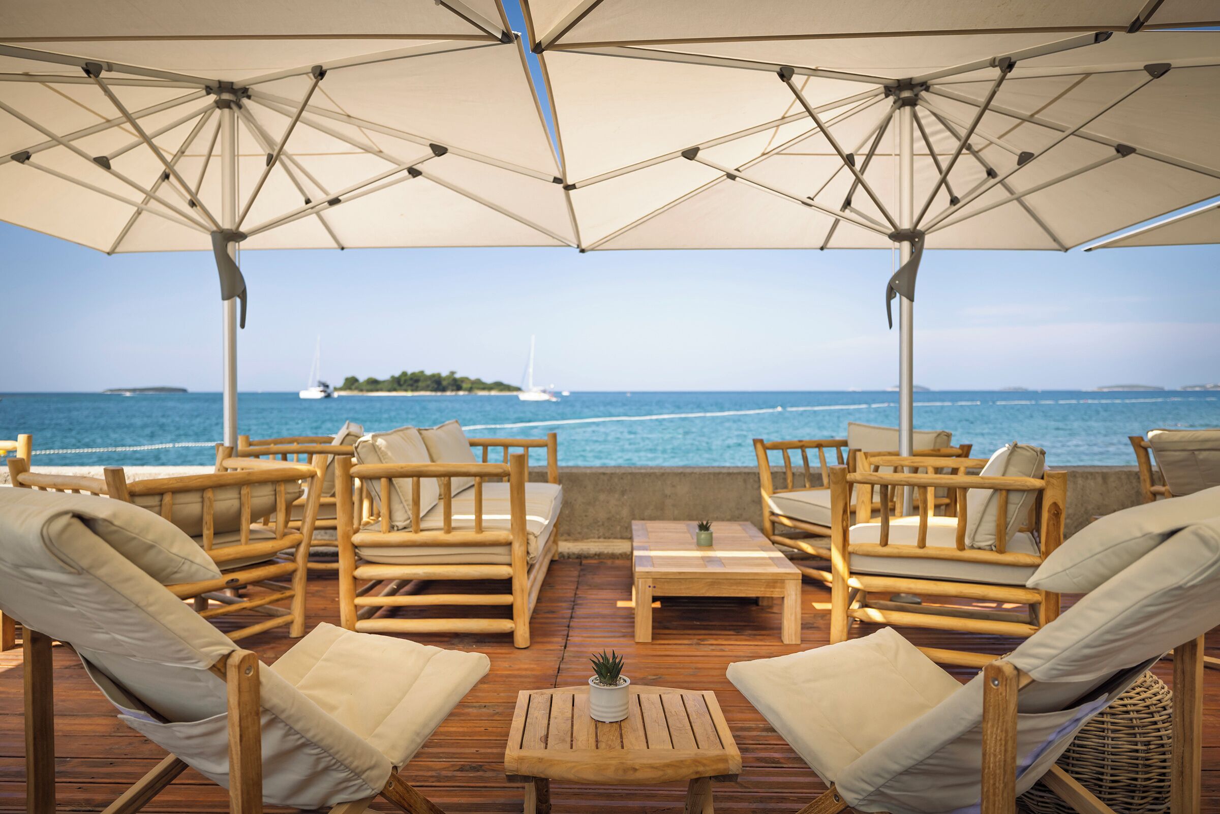 Une terrasse en bois, dotée de mobilier d’extérieur et de parasols, qui offre une vue sur la mer.
