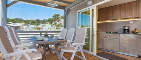 A covered outdoor dining area with a table and chairs, a kitchen with cabinets and appliances, and a view of the surrounding landscape.