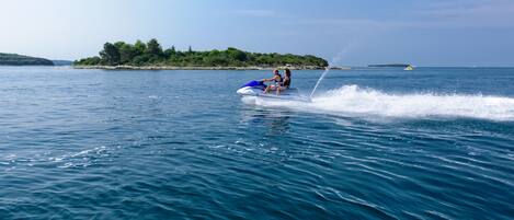 A person jet-skiing on a body of water with a distant island and trees in the background.