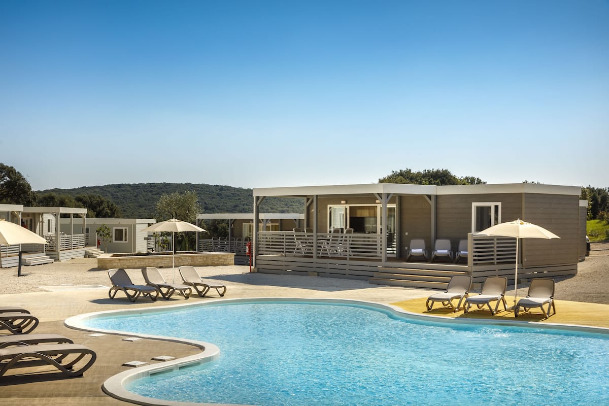 A pool area with lounge chairs and umbrellas, a covered seating area, and a view of the hills in the background.