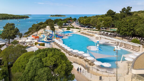 A resort with a large swimming pool, water slides, and a view of the sea.