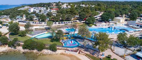 Luftaufnahme eines Küstenresorts mit großem Swimmingpool, Strandbereich und mehreren Gebäuden.