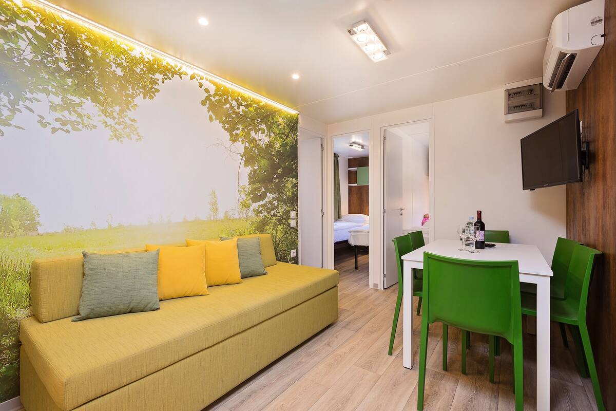 A modern room with a yellow sofa, green chairs, a white table, and a mural of a field.