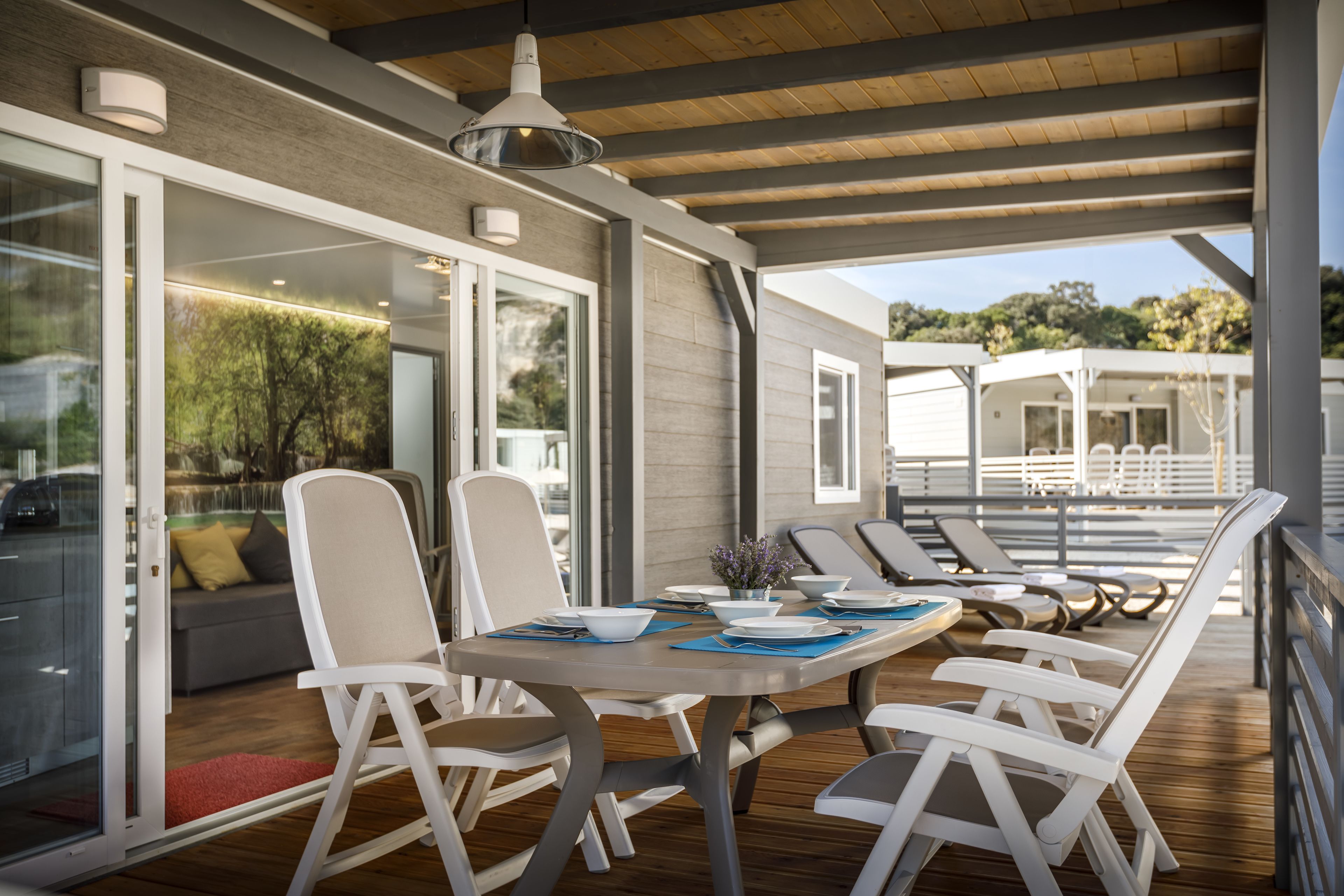 A modern outdoor dining area with a wooden deck, white chairs, and a table set for four.