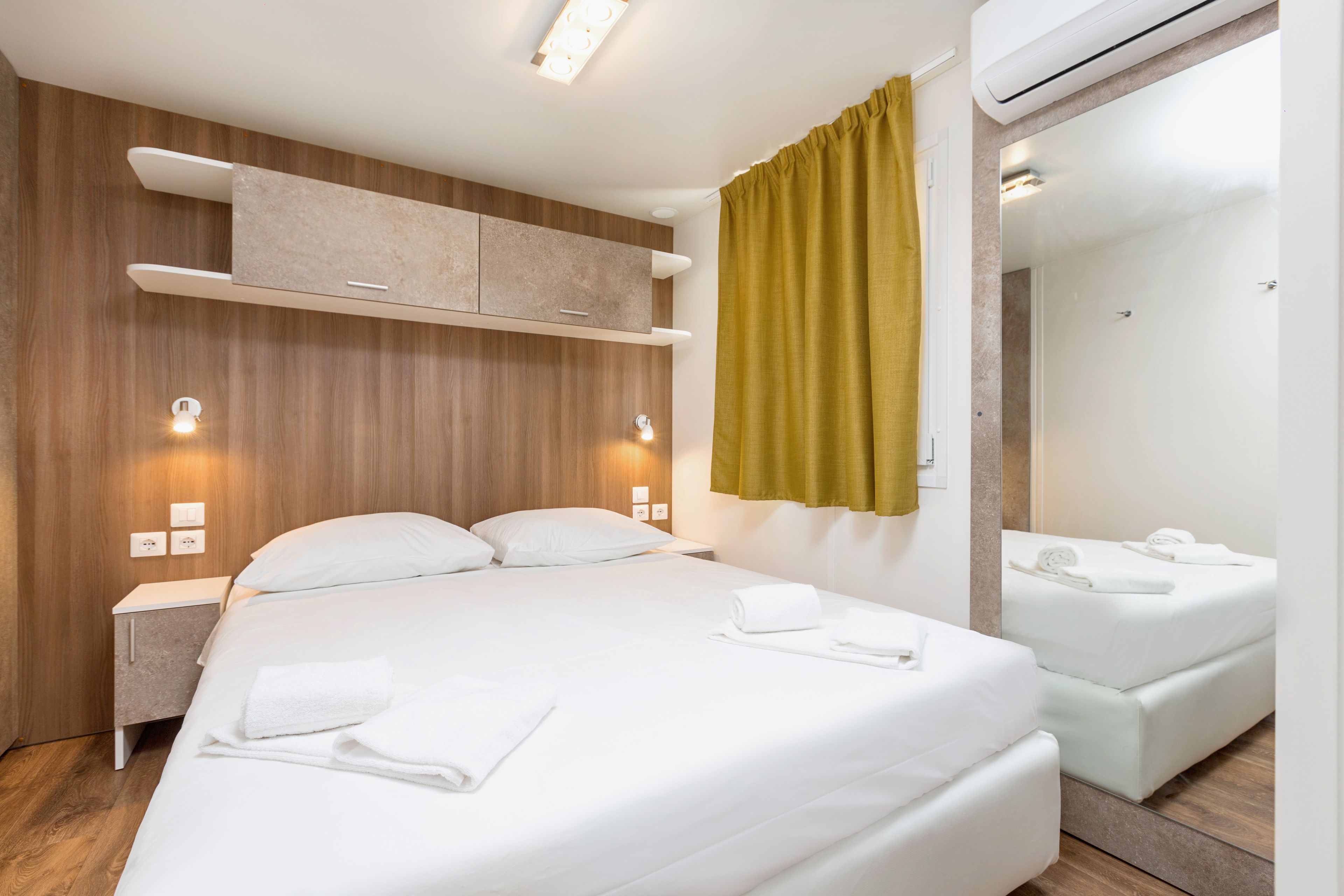 A hotel room with a bed, a nightstand, a mirror, and a wall-mounted shelf.