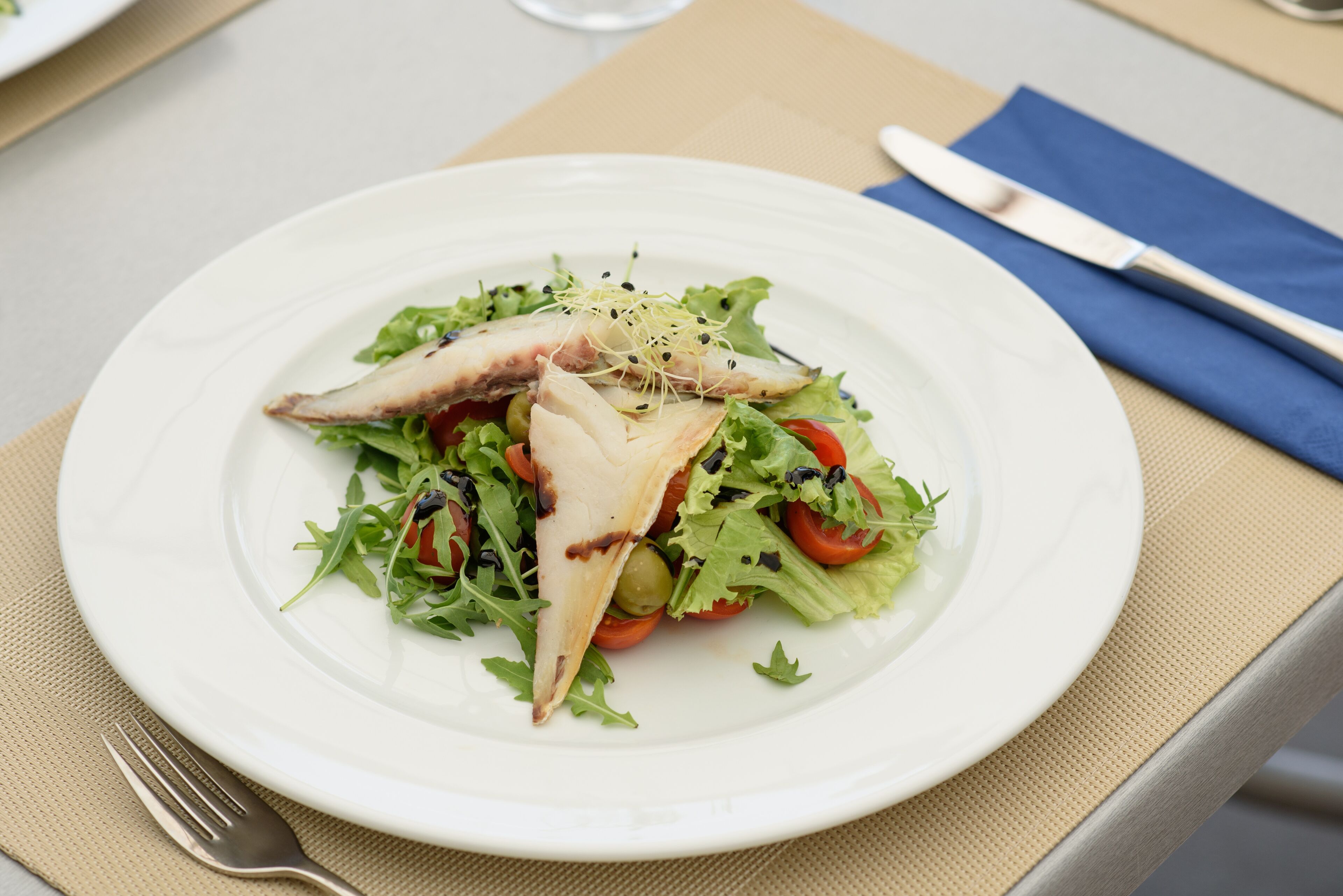 Un plato blanco con una ensalada de lechuga, tomates cherry y pollo a la parrilla, sobre un posavasos color beige.