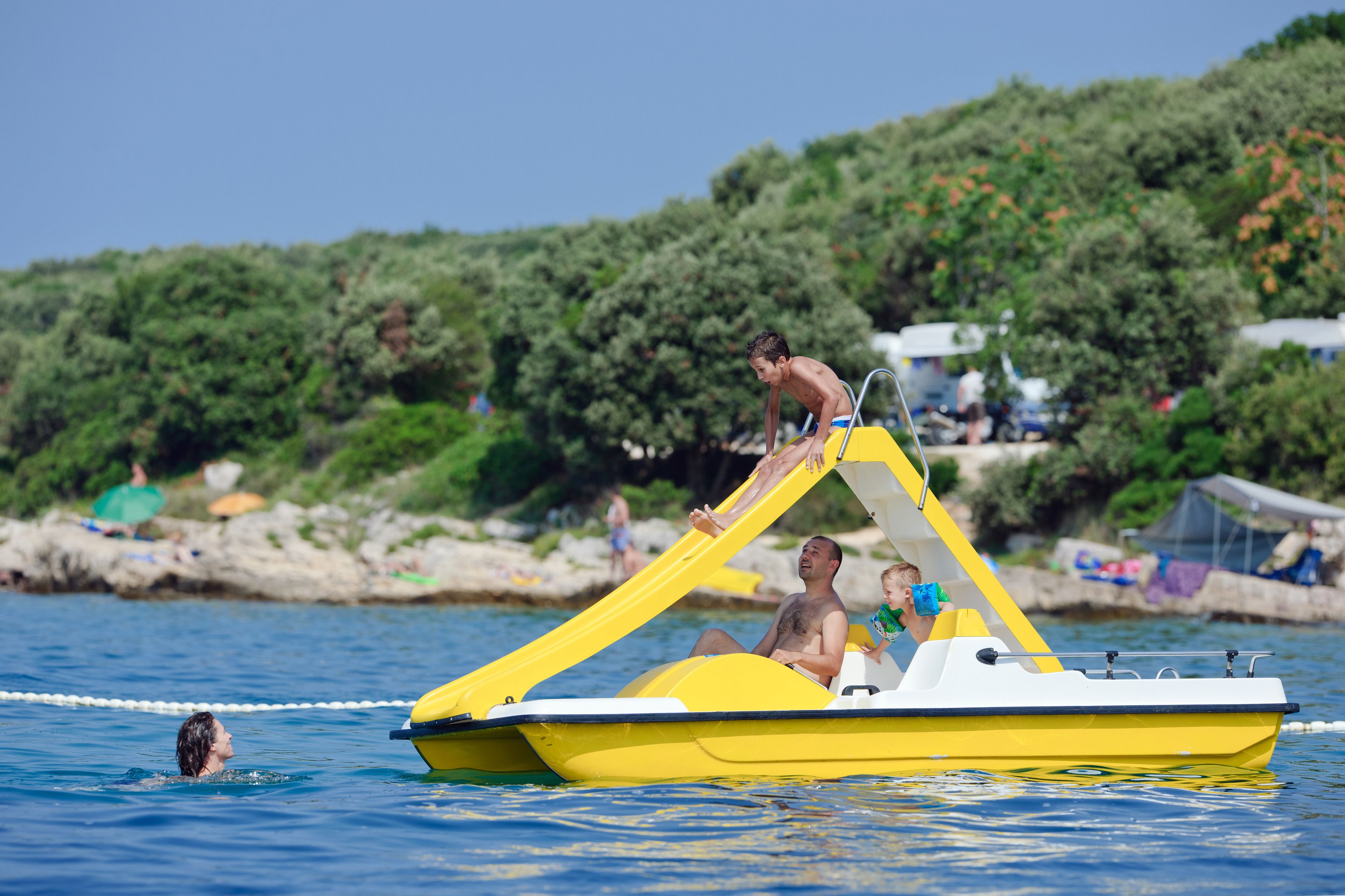 A yellow boat with a slide, a person climbing the slide, and another person sitting at the back.