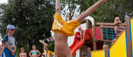 A person performing a handstand on a sandy surface with playground equipment in the background.